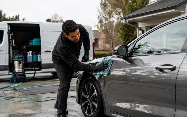 Mobile detailer cleaning a car with a service van nearby